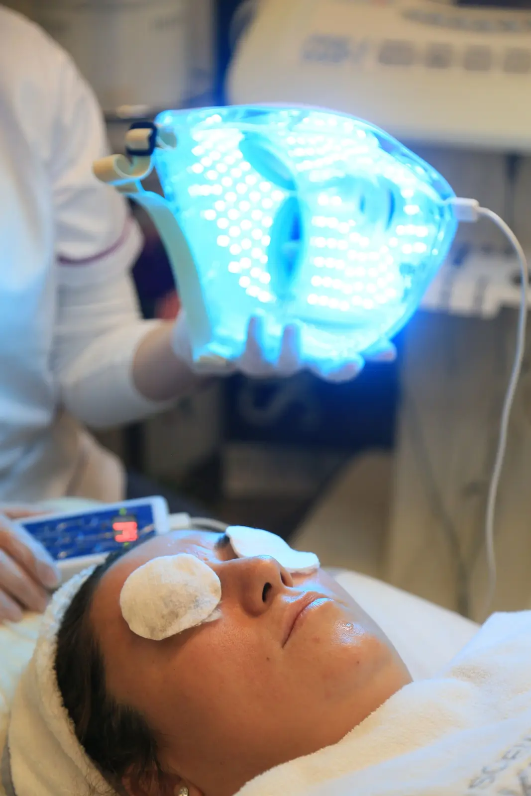 Esthéticienne plaçant un masque LED bleu sur le visage d'une cliente