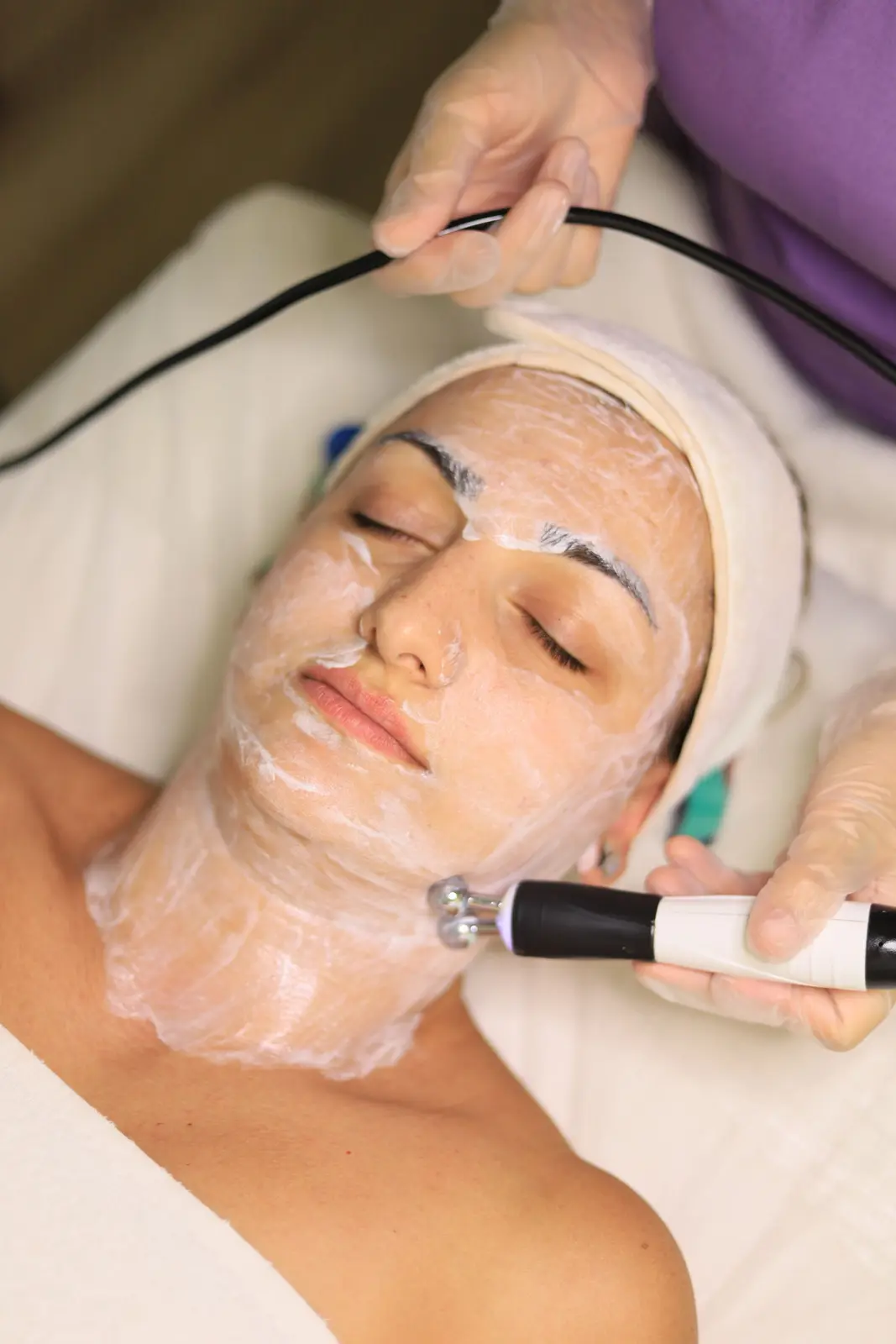 Cliente allongée avec un gel sur le visage pendant un soin avec une pièce à main